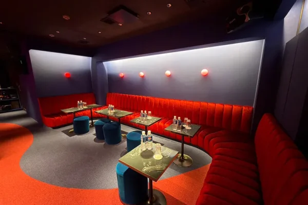 Curved red velvet sofa seating around small glass tables in a dim blue-walled lounge area.
