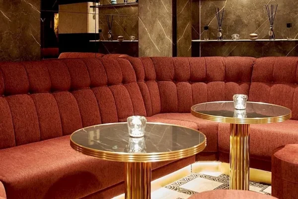 Red velvet curved sofa forming a lounge nook with two round glass-top tables and candleholders.