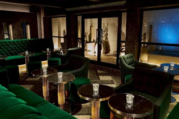 Luxurious lounge area with green velvet sofas, round marble tables, and candles in a dimly lit bar setting.
