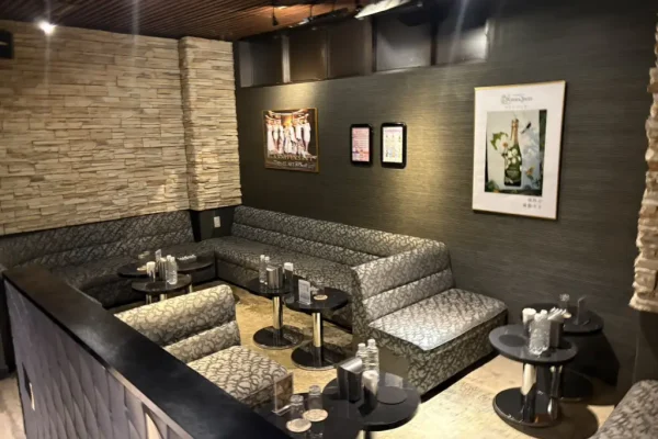 Cozy lounge area with L-shaped patterned booths, small round tables, and dim lighting along stone and dark walls with framed posters on the wall