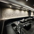 Dimly lit lounge area with black leather banquette seating and marble tables against a textured stone wall.