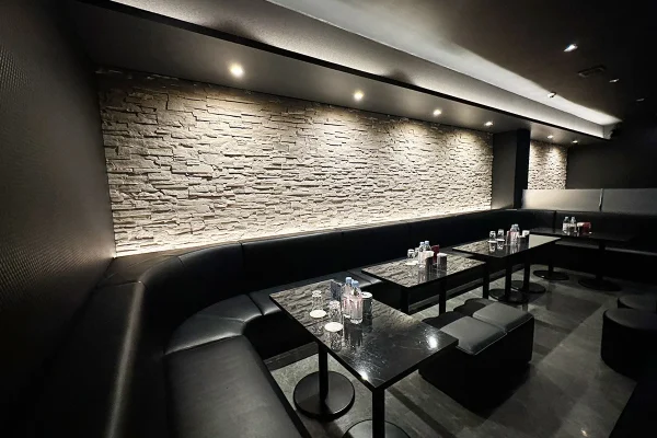 Dimly lit lounge area with black leather banquette seating and marble tables against a textured stone wall.