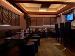 Cozy dimly lit bar lounge with wooden floors, low tables, and high chairs along a counter.