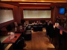 Dimly lit restaurant dining area with wooden floors, booths along the left, and tables set with glasses and napkins.