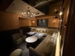 Dimly lit lounge with beige sectional seating around white oval coffee tables and chandeliers.