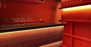 Red-lit bar interior featuring a curved counter with tiled front and warm under-counter lighting.
