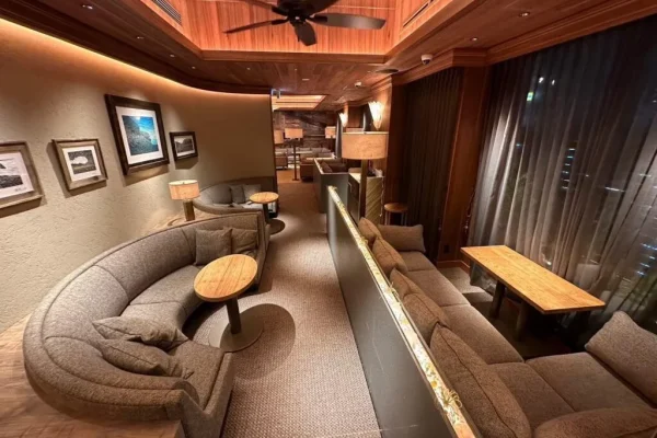 Cozy hotel lounge with a curved beige sectional, round wooden tables, lamps, and a wood-paneled ceiling.